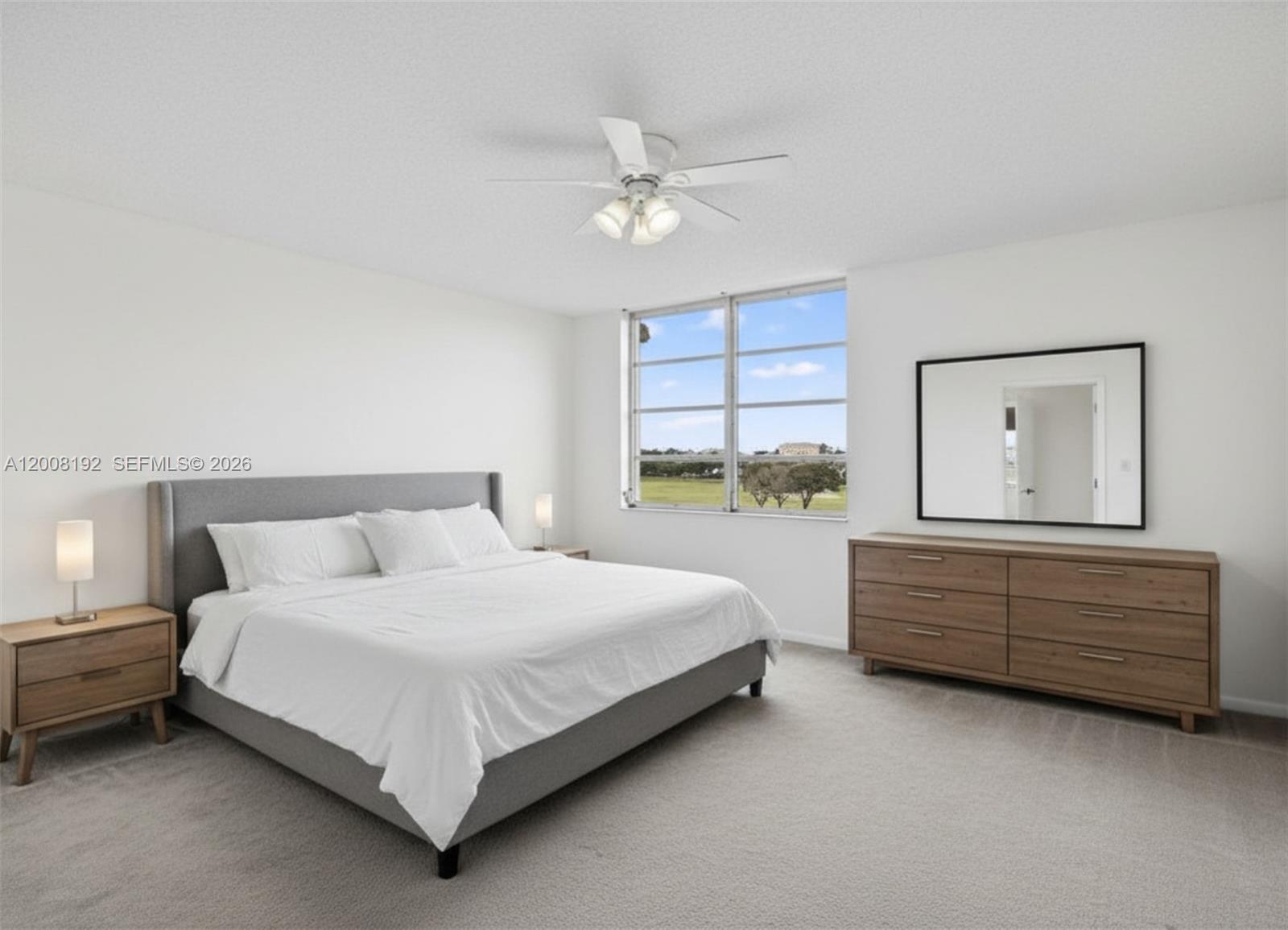 A bedroom features a gray upholstered bed, wooden furniture, and a window with outdoor views — 3300 W Rolling Hills Cir # 606, Davie FL 33328, DAVIE, FL