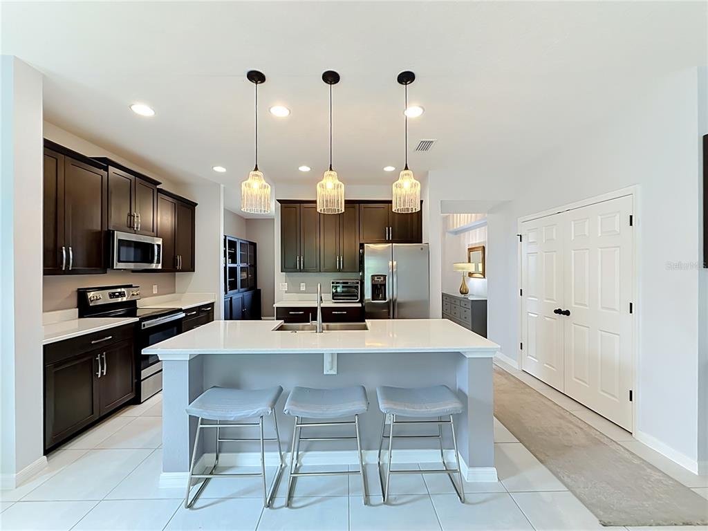 A kitchen features dark wood cabinets, a white quartz island with three stools, and pendant lighting — 5516 WINDSONG OAK DRIVE, LEESBURG, FL