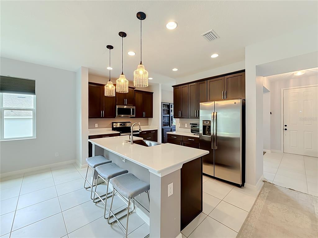 A modern kitchen features dark wood cabinets, stainless steel appliances, and a white quartz island — 5516 WINDSONG OAK DRIVE, LEESBURG, FL