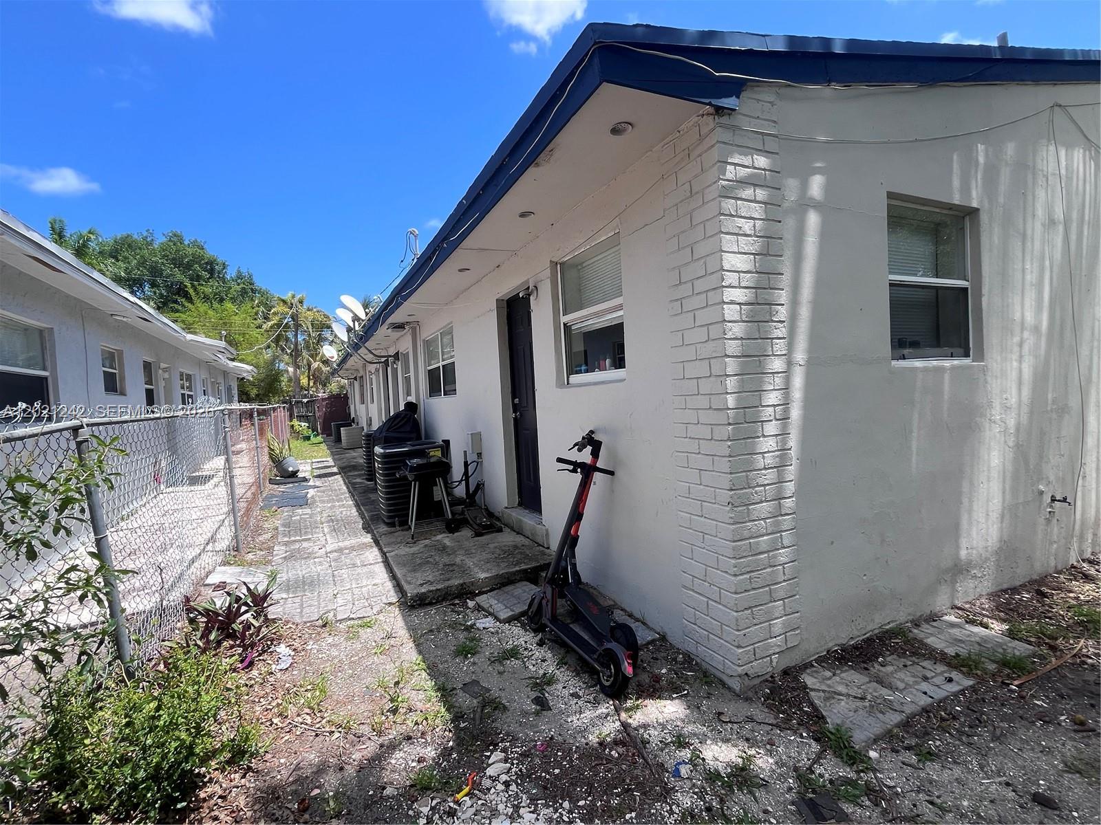 A side view of a white building with a brick corner and a parked electric scooter — 109 NW 14th Way # 4, Dania Beach FL 33004, DANIA BEACH, FL