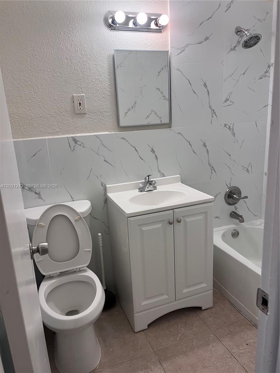 A small bathroom features a white vanity, a toilet, and a tub with marble-patterned tiles — 109 NW 14th Way # 4, Dania Beach FL 33004, DANIA BEACH, FL