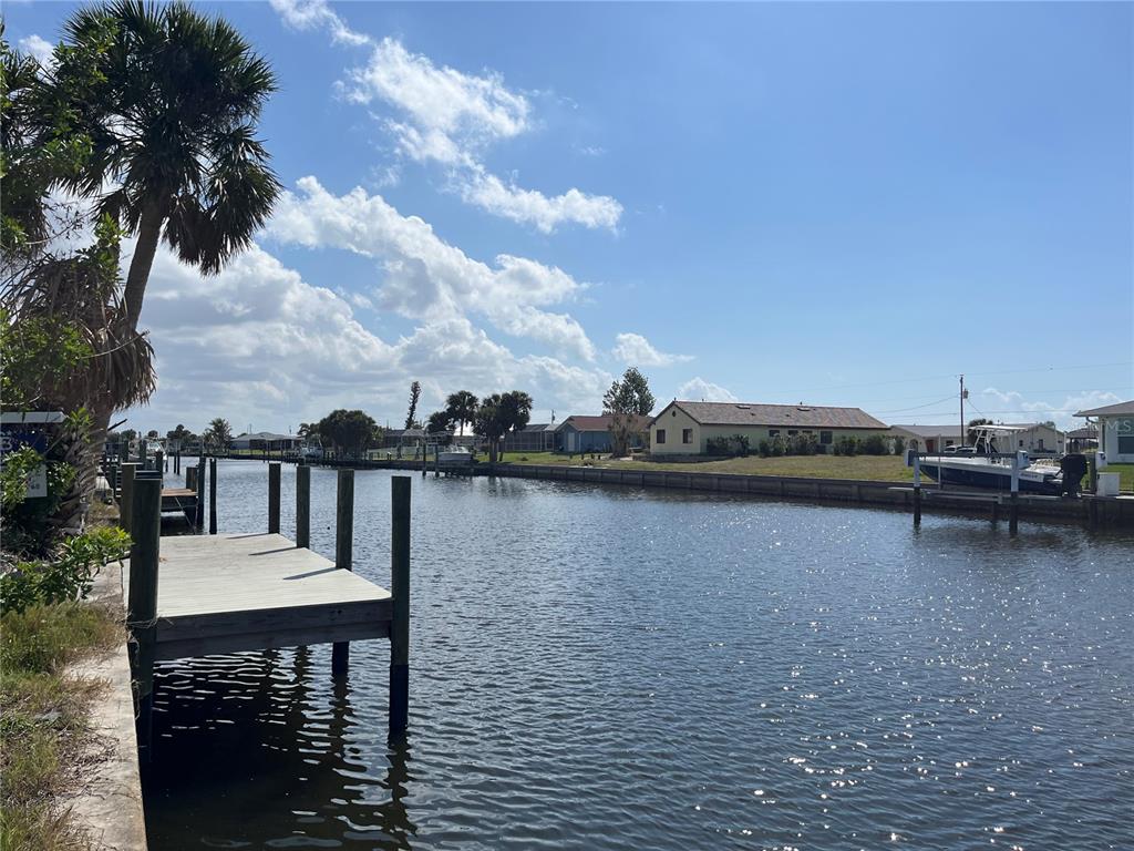 A wooden dock extends into a canal lined with houses and palm trees under blue skies — 21081 EDGEWATER DRIVE, PORT CHARLOTTE, FL