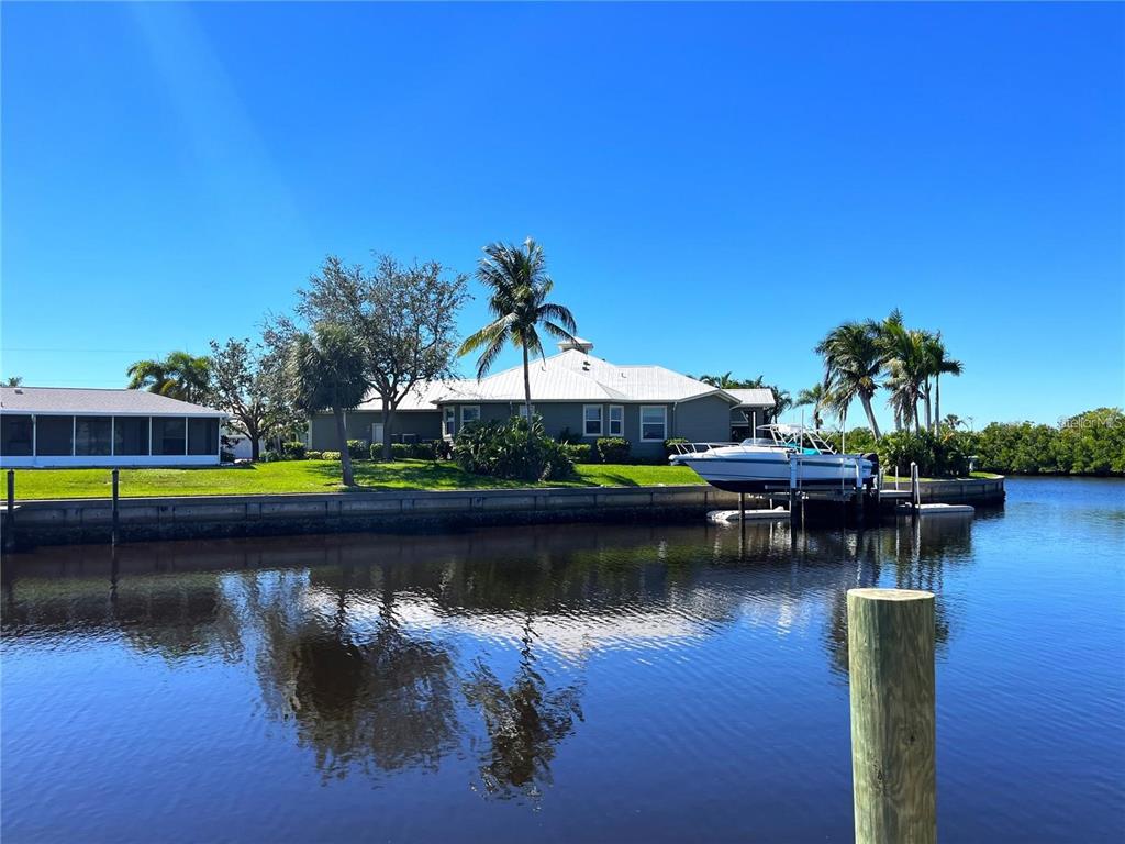 A waterfront house with a boat lift sits on a canal under a clear blue sky — 21081 EDGEWATER DRIVE, PORT CHARLOTTE, FL