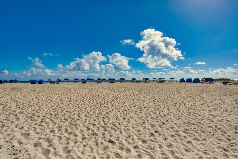 A wide, sandy beach features rows of blue umbrellas and cabanas under a sunny sky — 2800 N Ocean Drive, Riviera Beach FL 33404, RIVIERA BEACH, FL