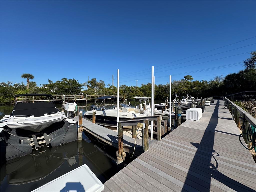 A wooden dock extends over water with several boats moored in a sunny outdoor setting — 707 SORRENTO INLET UNIT 707, NOKOMIS, FL