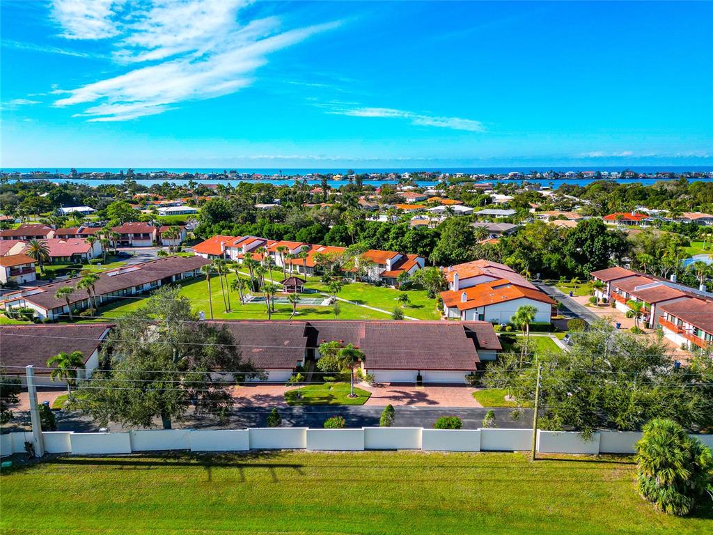 An aerial view of a residential complex with brown-roofed buildings, green lawns, and distant water — 707 SORRENTO INLET UNIT 707, NOKOMIS, FL