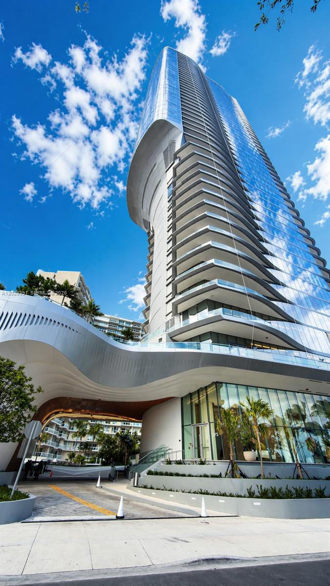 A modern, curved glass high-rise building features a prominent white architectural canopy over the entrance — 174 SE 25 RD # 504, Miami FL 33131, MIAMI, FL