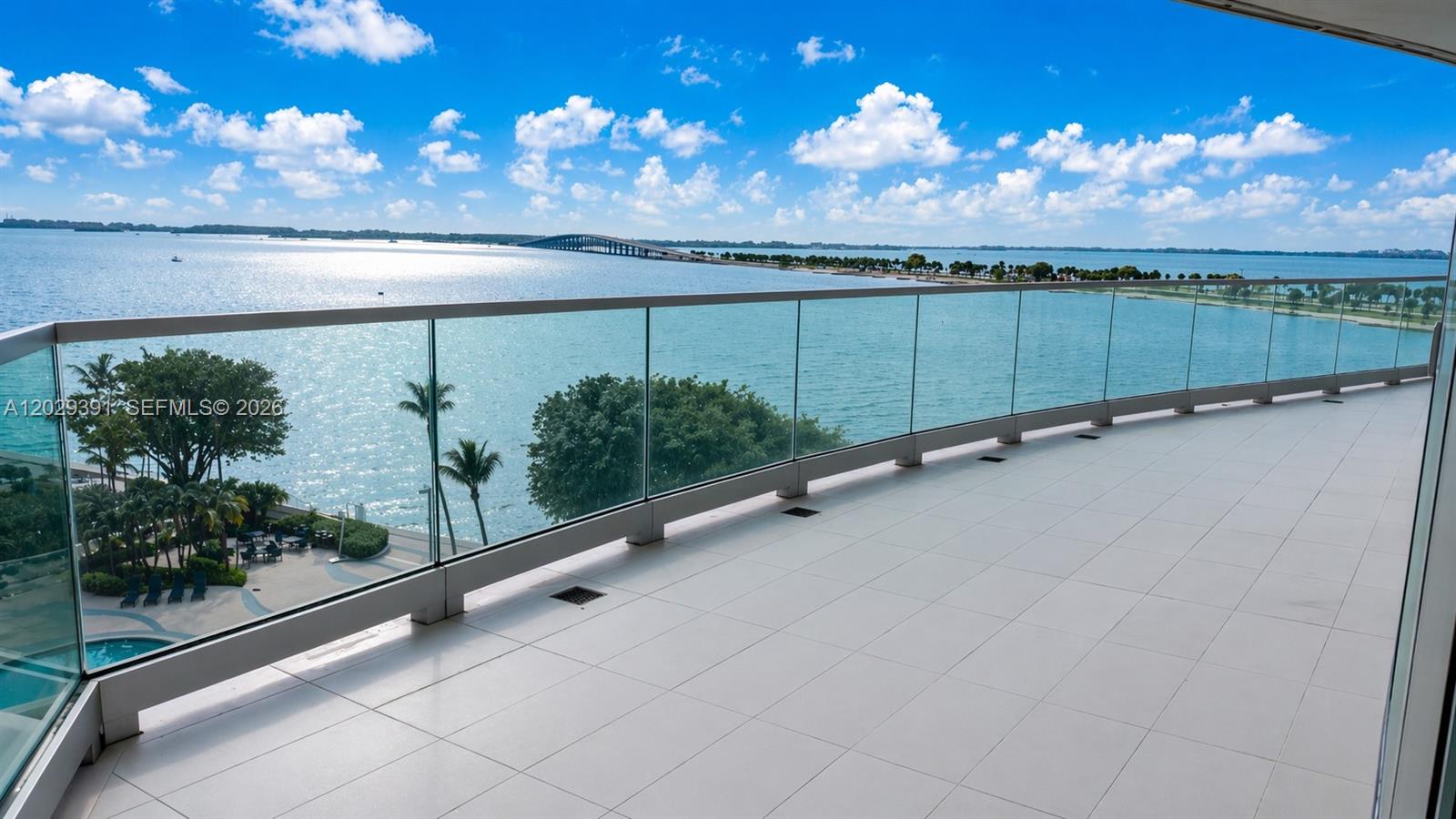 A spacious balcony with glass railings overlooks a bay and a distant bridge — 174 SE 25 RD # 504, Miami FL 33131, MIAMI, FL