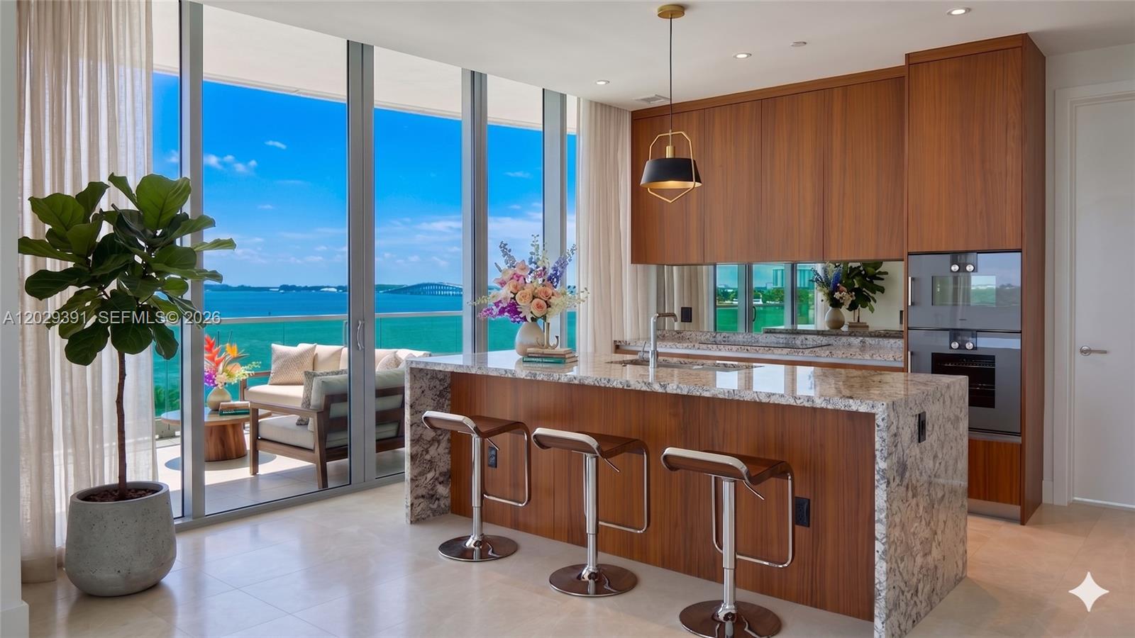A modern kitchen with wood cabinetry, granite island, and floor-to-ceiling windows overlooking the ocean — 174 SE 25 RD # 504, Miami FL 33131, MIAMI, FL