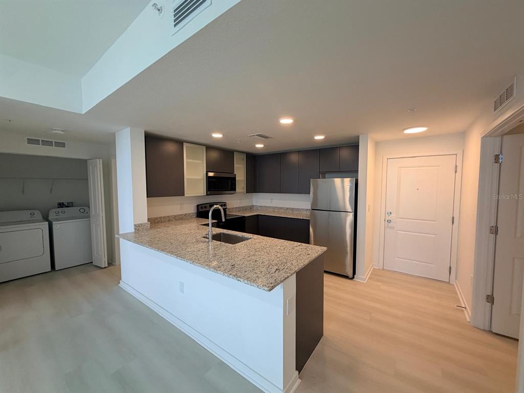A kitchen features granite countertops, dark cabinetry, stainless steel appliances, and an adjacent laundry closet — 5587 MILLENIA PARK BOULEVARD UNIT 510, ORLANDO, FL
