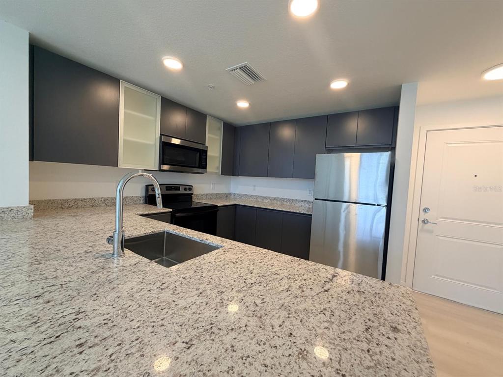 A kitchen features dark cabinets, granite countertops, stainless steel appliances, and a peninsula sink — 5587 MILLENIA PARK BOULEVARD UNIT 510, ORLANDO, FL