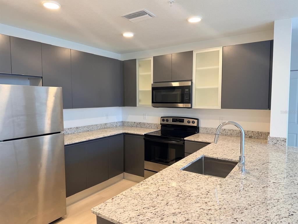 A modern kitchen features dark gray flat-panel cabinets, granite countertops, and stainless steel appliances — 5587 MILLENIA PARK BOULEVARD UNIT 510, ORLANDO, FL