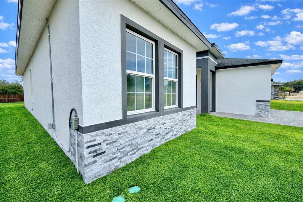 A side view of a modern house exterior featuring white stucco, stone veneer, and windows — 11591 SW 59TH TERRACE, OCALA, FL