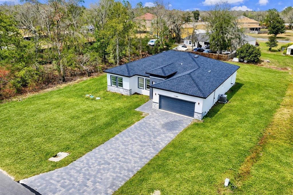 An aerial view of a modern single-story house with a dark roof and paved driveway — 11591 SW 59TH TERRACE, OCALA, FL