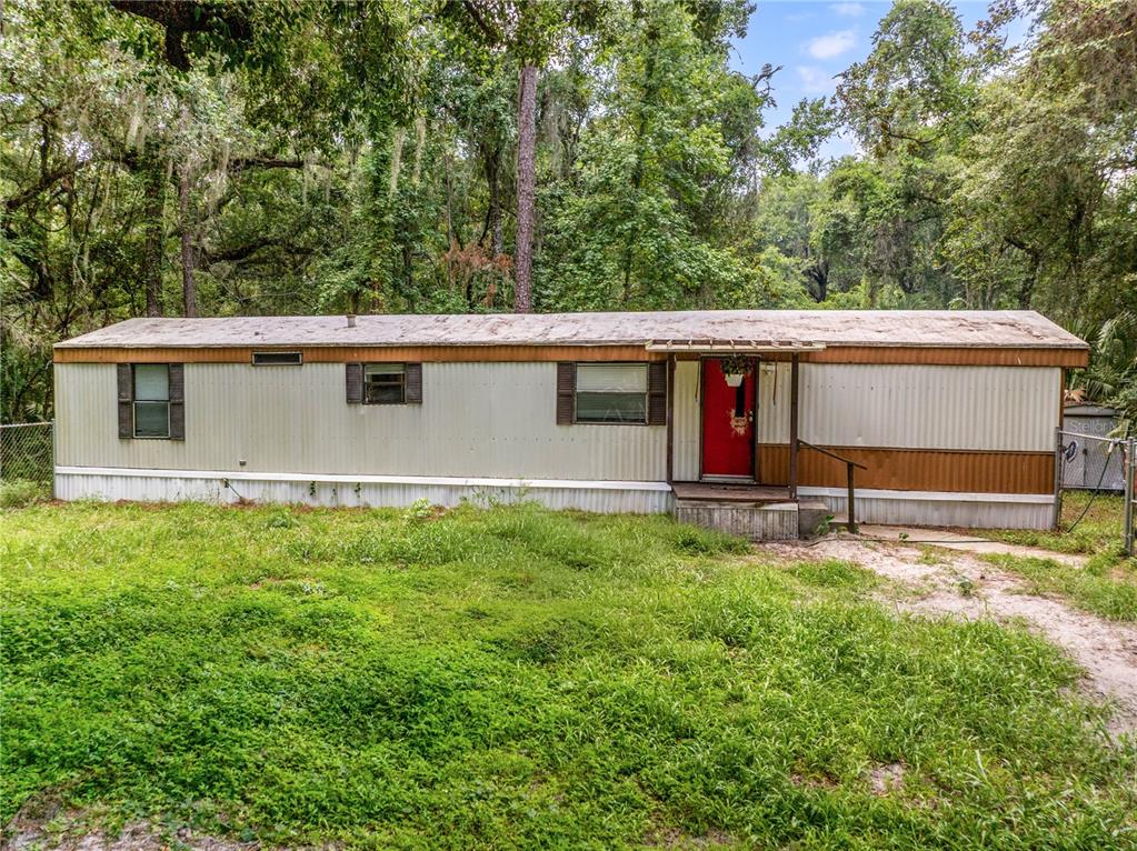 A single-wide mobile home with a red front door sits on a grassy lot — 3080 CR 417, LAKE PANASOFFKEE, FL