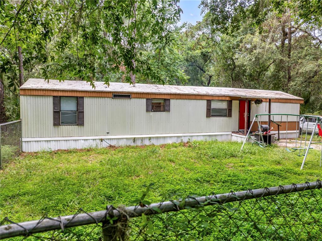 A single-story mobile home with beige siding sits in a grassy, fenced-in yard — 3080 CR 417, LAKE PANASOFFKEE, FL