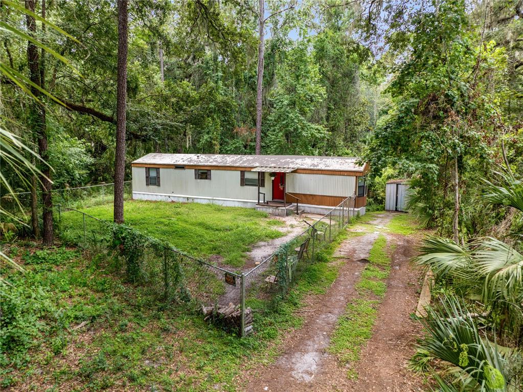 A single-story mobile home sits on a grassy lot surrounded by trees and a fence — 3080 CR 417, LAKE PANASOFFKEE, FL