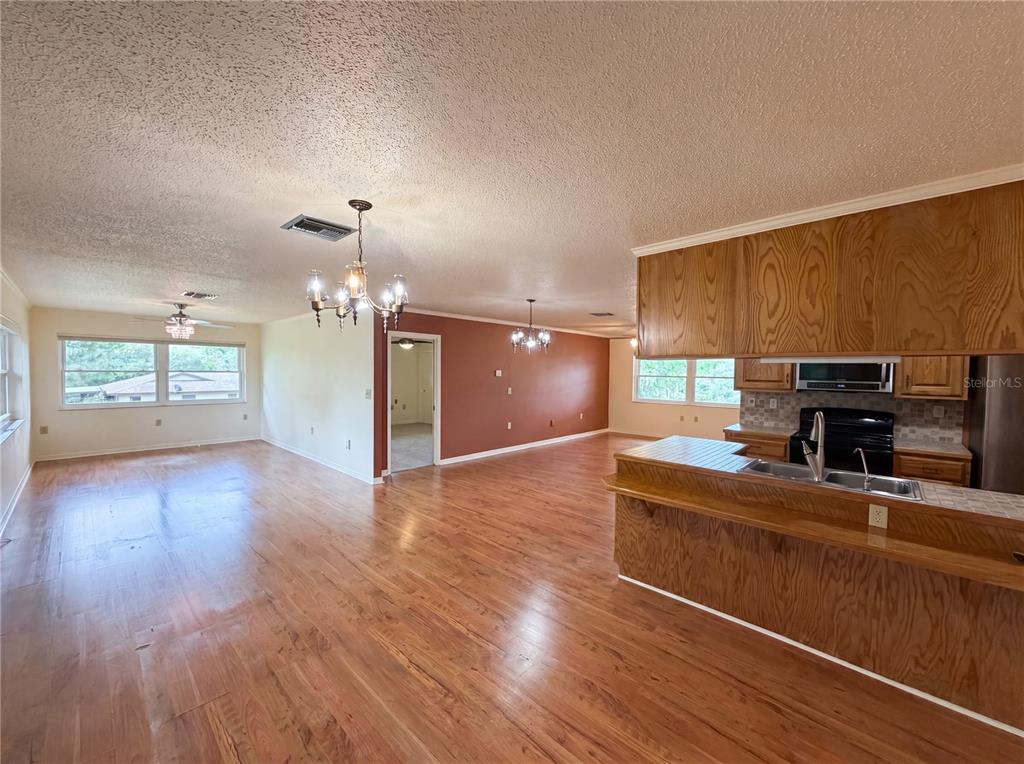 An open-concept living and dining area features wood flooring, wood cabinetry, and a kitchen island — 1641 S VALERIE POINT, INVERNESS, FL