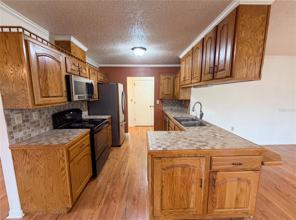 A kitchen features oak cabinets, tiled countertops, stainless steel appliances, and wood-look flooring — 1641 S VALERIE POINT, INVERNESS, FL