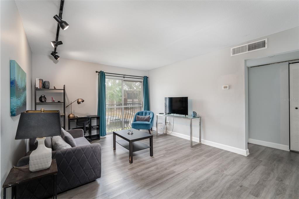 A living room features gray wood-look flooring, a sofa, a desk, and a sliding glass door — 1700 SW 16TH COURT UNIT C25, GAINESVILLE, FL