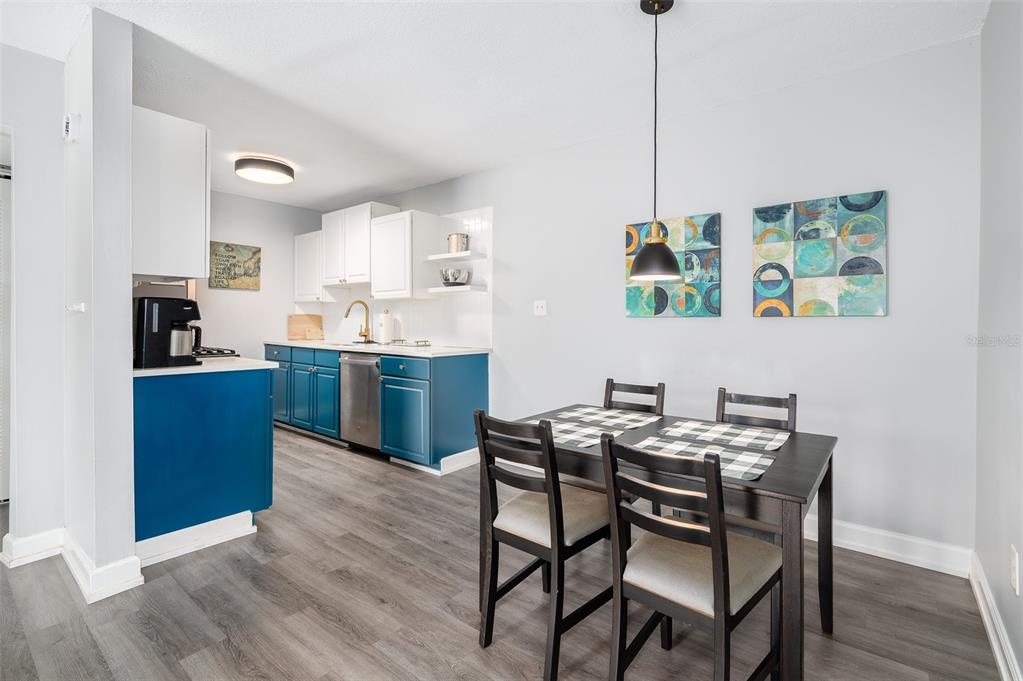 A kitchen and dining area featuring blue lower cabinets, white upper cabinets, and dark furniture — 1700 SW 16TH COURT UNIT C25, GAINESVILLE, FL