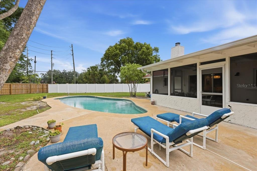 A backyard features a swimming pool, a screened-in patio, and lounge chairs on a concrete deck — 8495 CARAWAY COURT, ORLANDO, FL