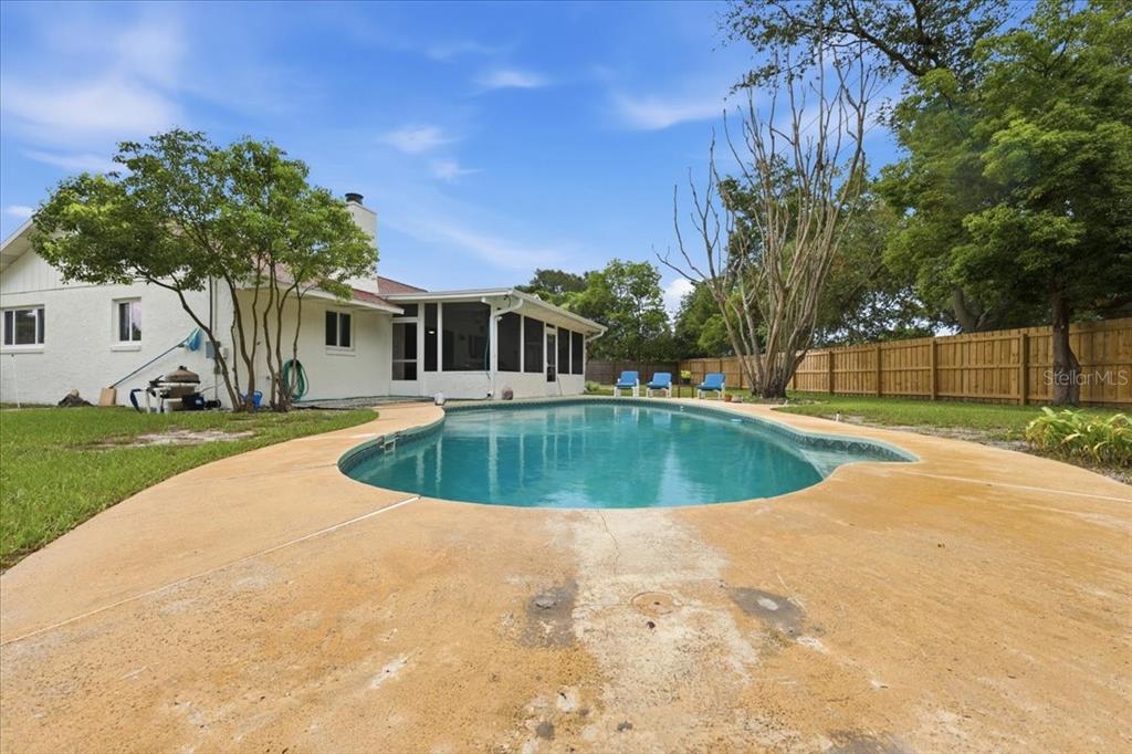 A backyard features a swimming pool, a concrete deck, and a white house with a porch — 8495 CARAWAY COURT, ORLANDO, FL
