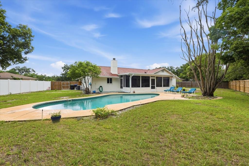 A backyard features a swimming pool, a screened-in porch, and a white house exterior — 8495 CARAWAY COURT, ORLANDO, FL