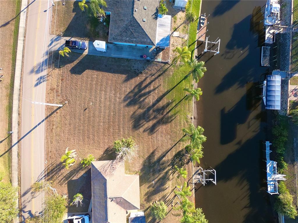 An aerial view shows a vacant waterfront lot situated between two houses along a canal — 27193 VOYAGEUR DRIVE, PUNTA GORDA, FL