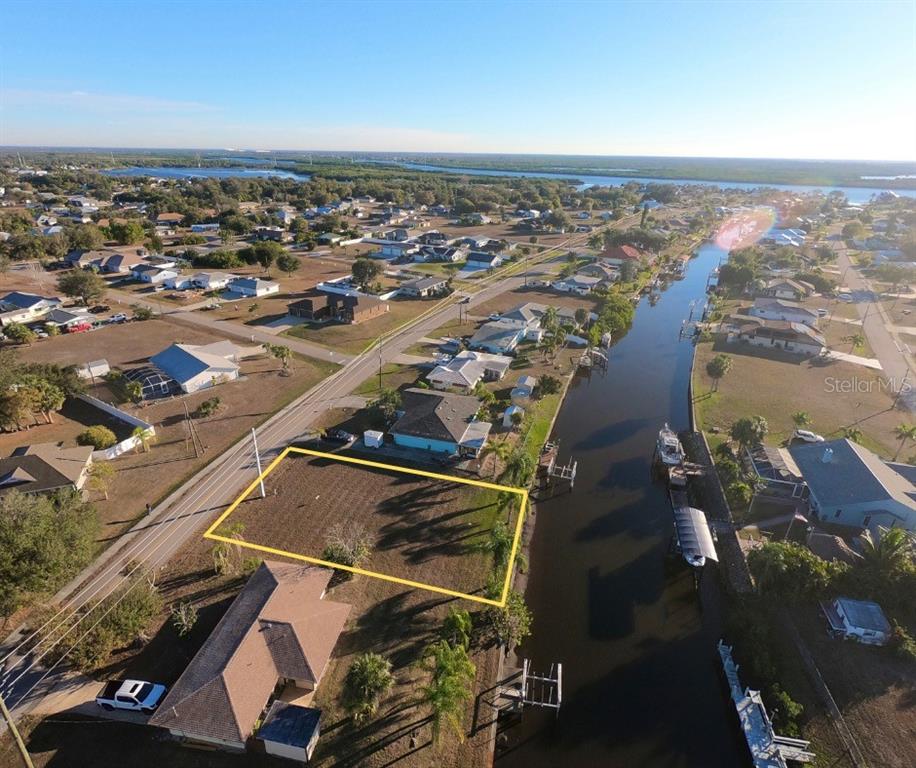 An aerial view shows a vacant waterfront lot outlined in yellow next to a canal — 27193 VOYAGEUR DRIVE, PUNTA GORDA, FL