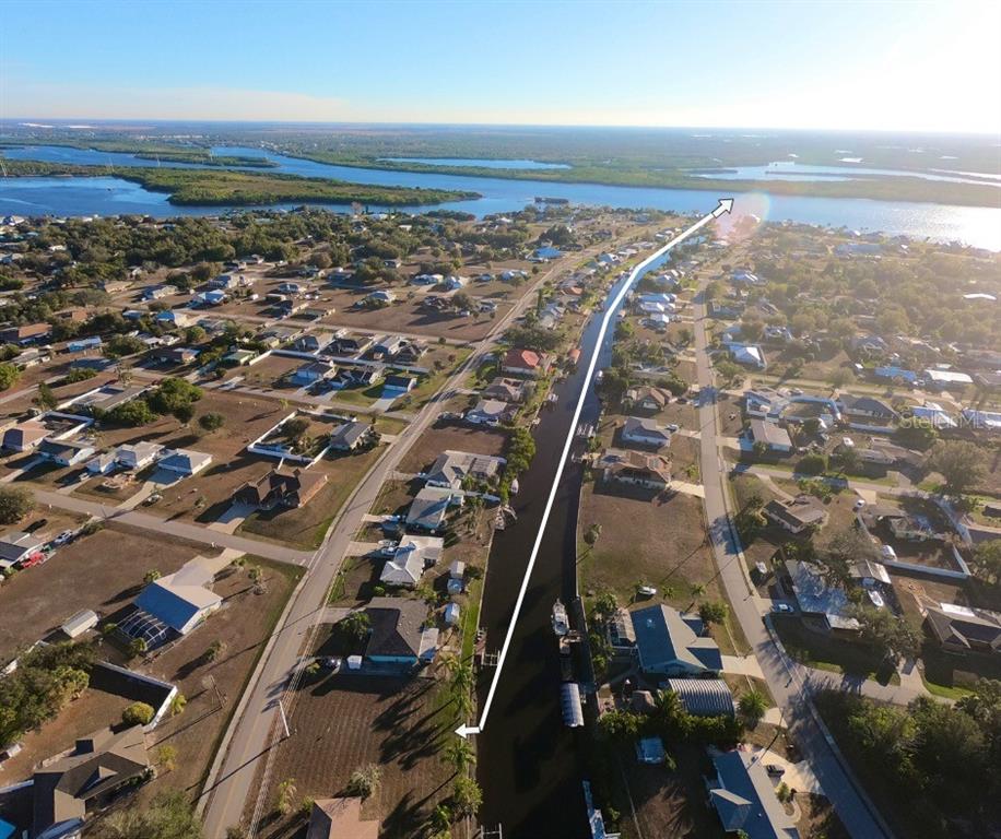 An aerial view shows a residential neighborhood with a canal leading toward a large body — 27193 VOYAGEUR DRIVE, PUNTA GORDA, FL