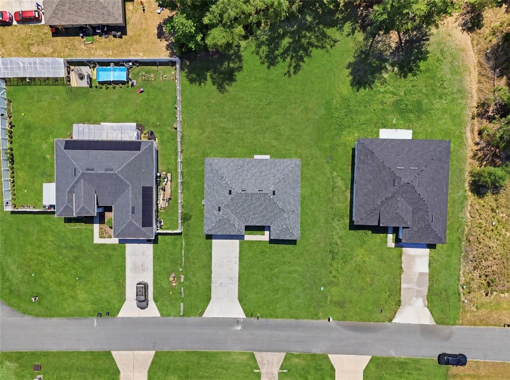 An aerial view shows three houses with dark roofs and concrete driveways along a street — 16843 SW 18TH AVENUE ROAD, OCALA, FL