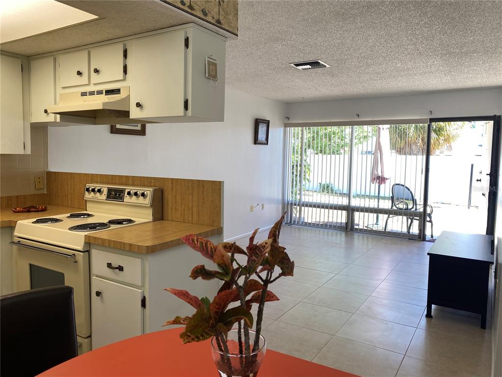 A kitchen with white cabinets and a stove overlooks a tiled living area with sliding doors — 4377 TAHITIAN GARDENS CIRCLE UNIT G, HOLIDAY, FL