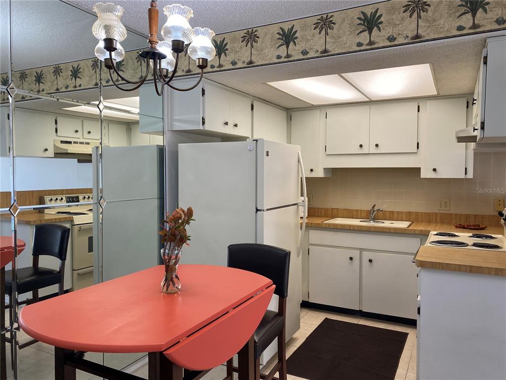 A kitchen with white cabinets, wood-look laminate countertops, a mirrored wall, and a dining table — 4377 TAHITIAN GARDENS CIRCLE UNIT G, HOLIDAY, FL