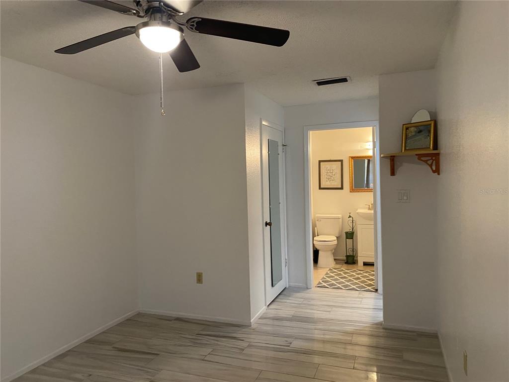 A room with light wood-look tile flooring leads to an adjacent bathroom with a toilet — 4377 TAHITIAN GARDENS CIRCLE UNIT G, HOLIDAY, FL