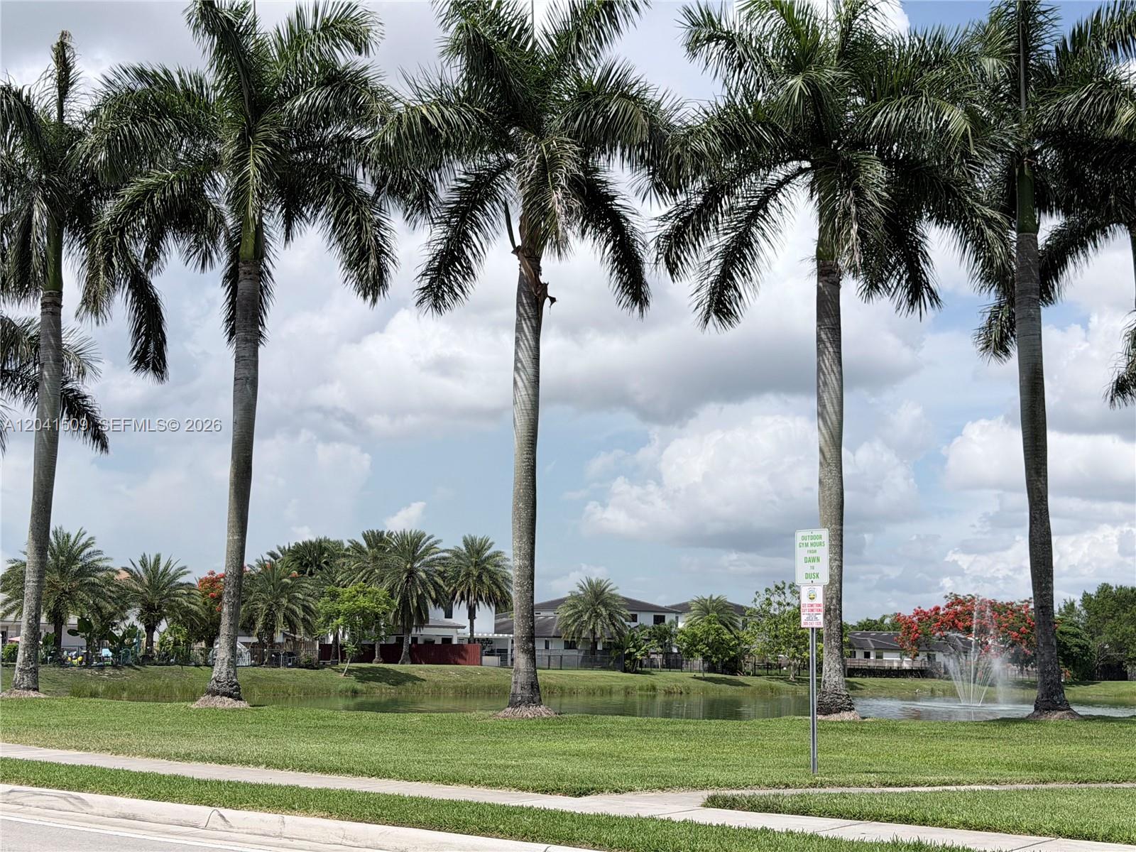 A row of tall palm trees stands along a grassy lawn overlooking a small lake — 268 SE 31st Ave, Homestead FL 33033, HOMESTEAD, FL