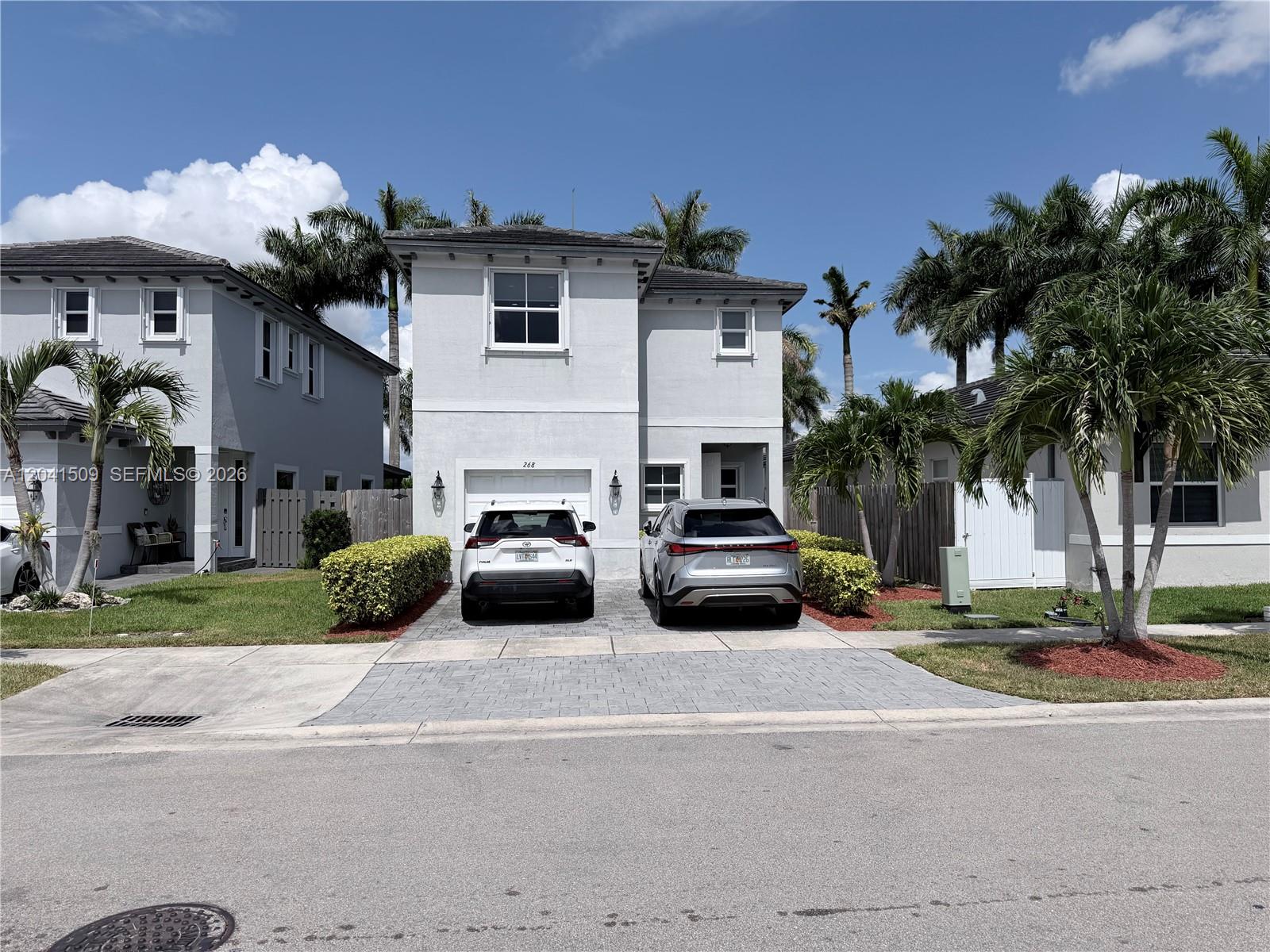 A two-story house with a paved driveway and two parked cars under a blue sky — 268 SE 31st Ave, Homestead FL 33033, HOMESTEAD, FL