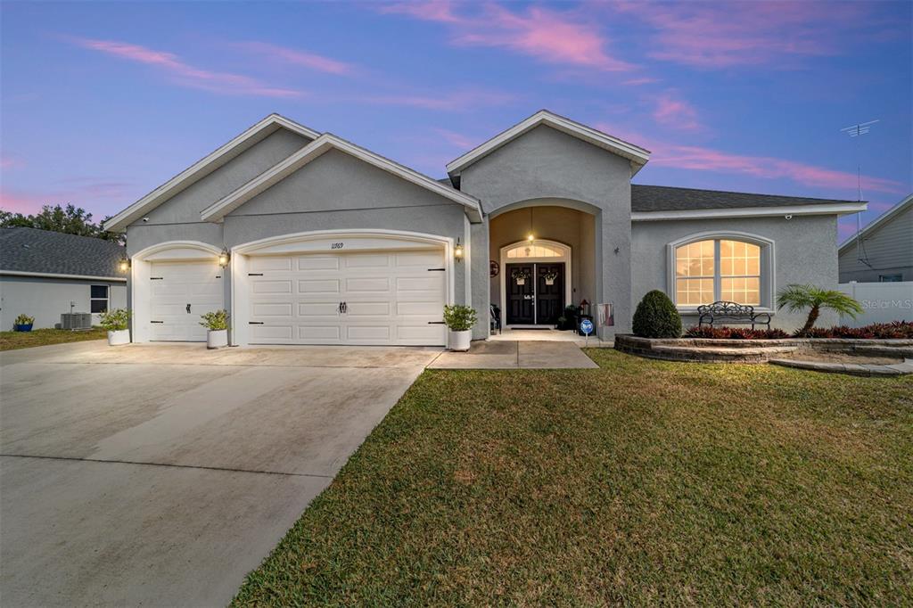 A single-story gray stucco house with a three-car garage and a front arched entryway — 11769 SW 60TH COURT, OCALA, FL