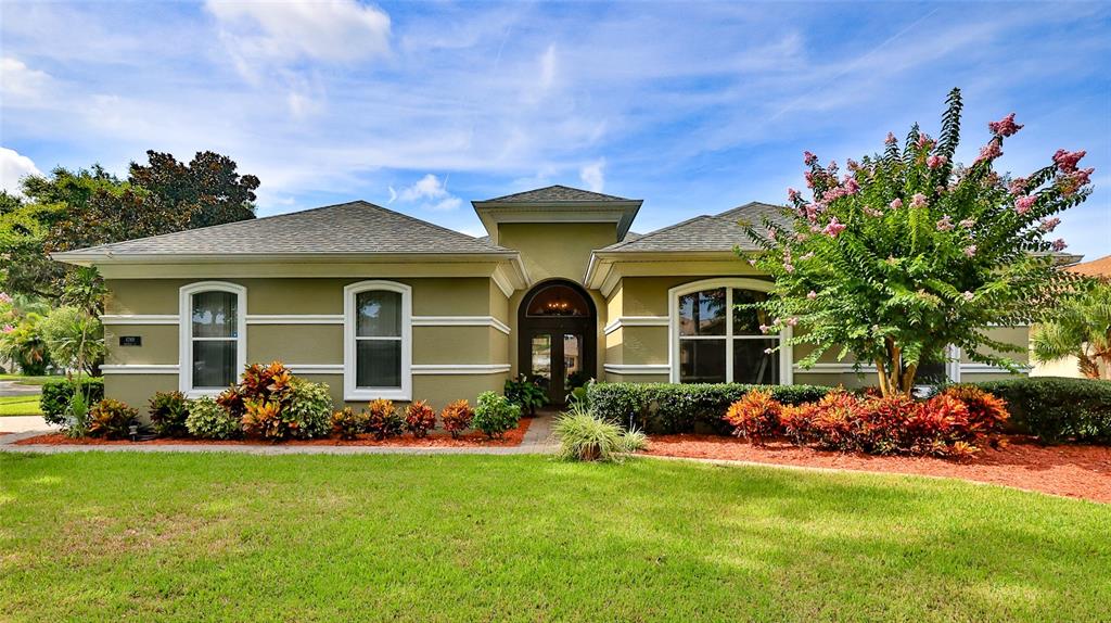 A single-story house with olive-green stucco walls, a central arched entryway, and landscaped front gardens — 4269 MAYFAIR LANE, PORT ORANGE, FL