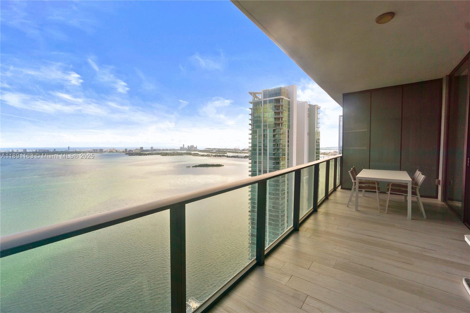 A high-rise balcony features a glass railing, tiled flooring, and a view of the bay — 480 NE 31st St # 4206, Miami FL 33137, MIAMI, FL