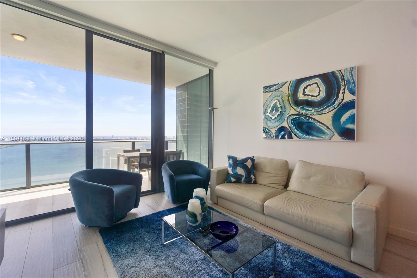 A living room features a white sofa, two blue armchairs, and a balcony overlooking water — 480 NE 31st St # 4206, Miami FL 33137, MIAMI, FL
