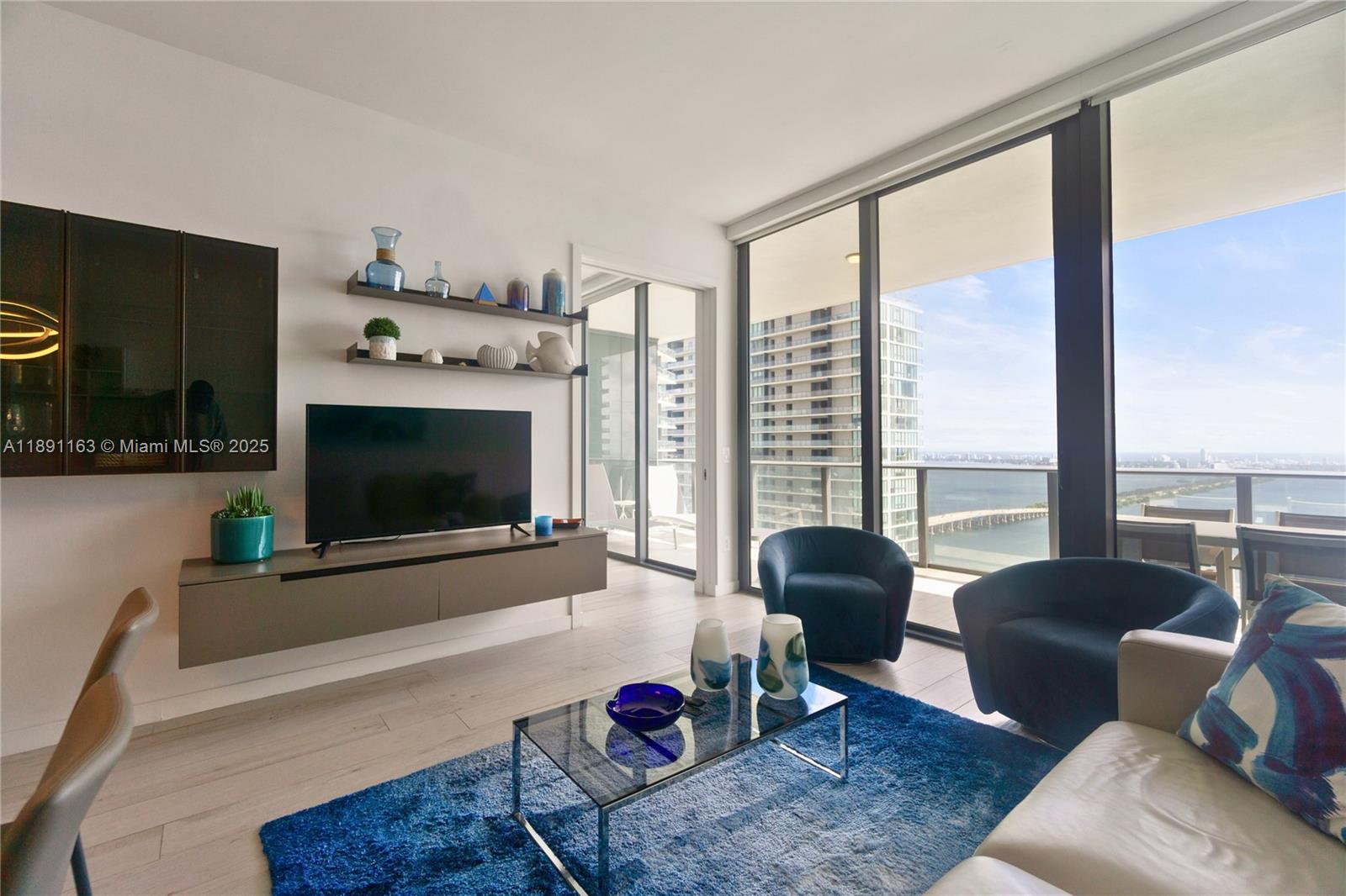 A modern living room features a blue rug, glass coffee table, and floor-to-ceiling windows — 480 NE 31st St # 4206, Miami FL 33137, MIAMI, FL
