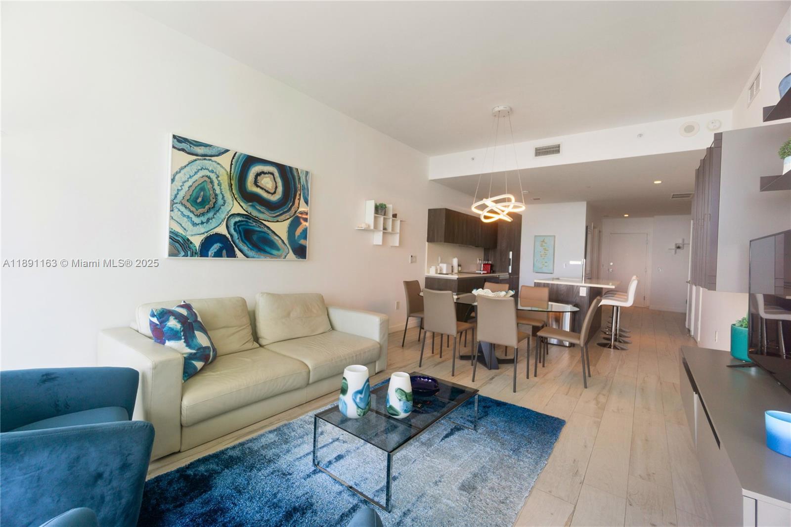 A modern living and dining area features a blue rug, leather sofa, and kitchen island — 480 NE 31st St # 4206, Miami FL 33137, MIAMI, FL