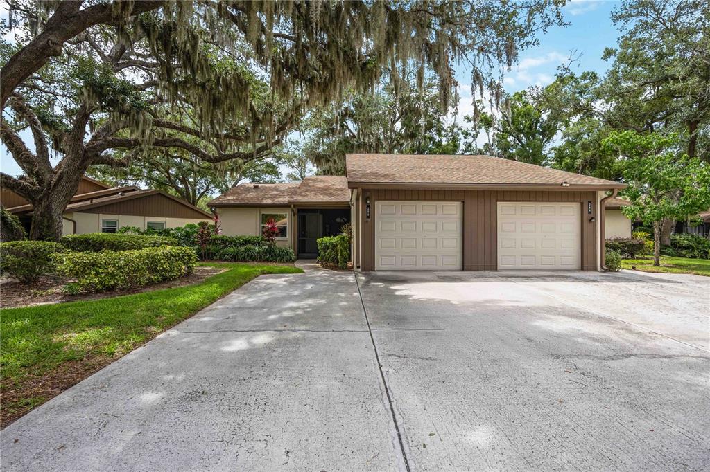 A single-story house with a two-car garage and large oak trees in the front yard — 266 OAK HILL DRIVE UNIT 34, SARASOTA, FL