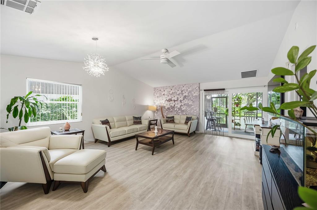 A bright living room features light wood flooring, white leather furniture, and a floral accent wall — 266 OAK HILL DRIVE UNIT 34, SARASOTA, FL