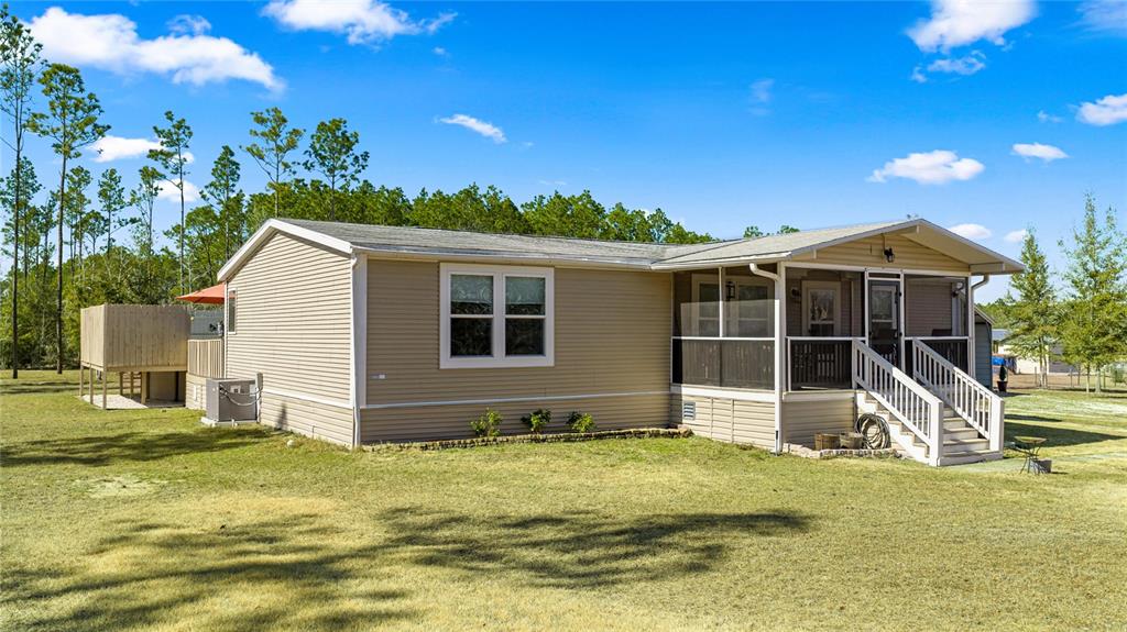 A tan manufactured home features a screened-in front porch and a wooden privacy deck — 5130 SE 137TH AVENUE, MORRISTON, FL