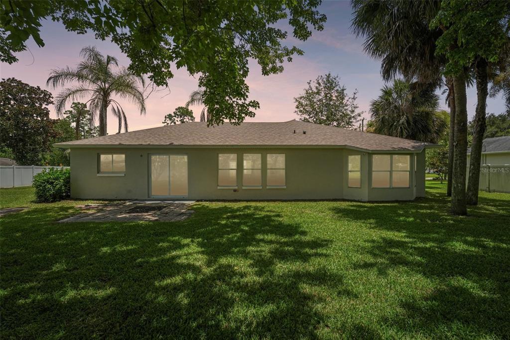 The rear exterior of a single-story house features a lawn, patio, and mature trees — 19 EMERSON DRIVE, PALM COAST, FL