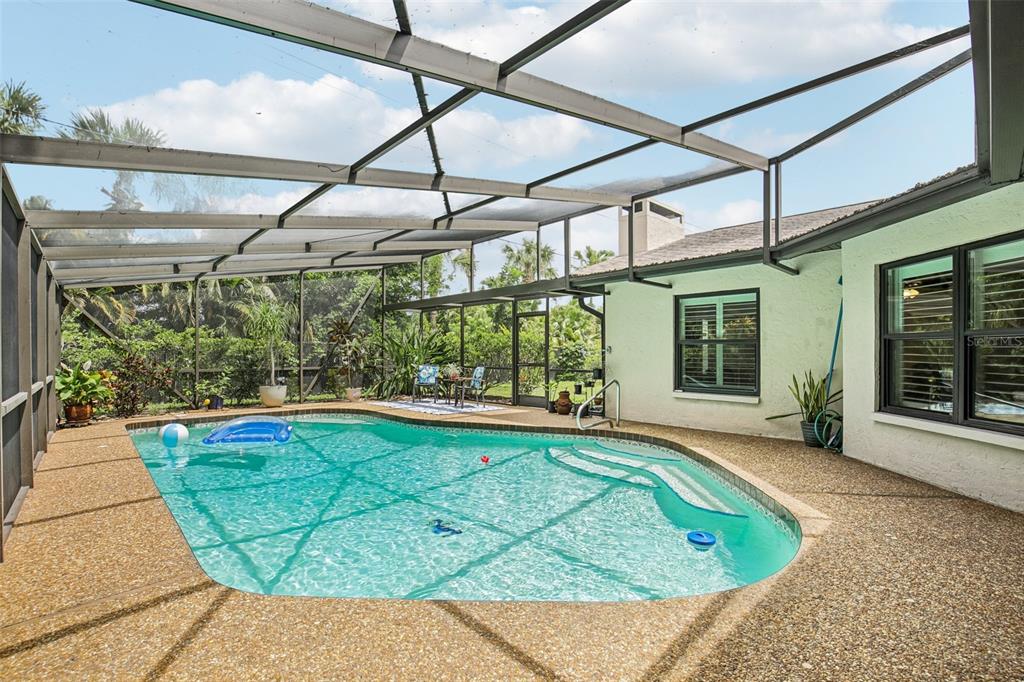 A screened-in swimming pool with a textured deck sits beside a white house exterior — 4541 CHARING CROSS ROAD, SARASOTA, FL