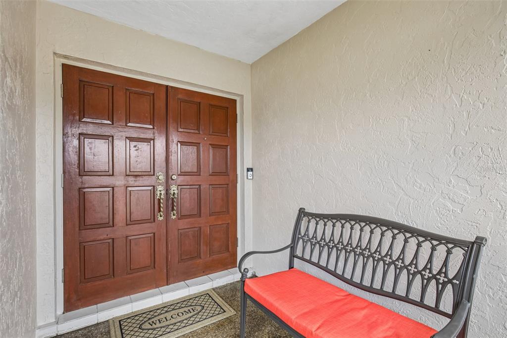A covered entryway features double wooden doors, a metal bench with an orange cushion, and flooring — 4541 CHARING CROSS ROAD, SARASOTA, FL