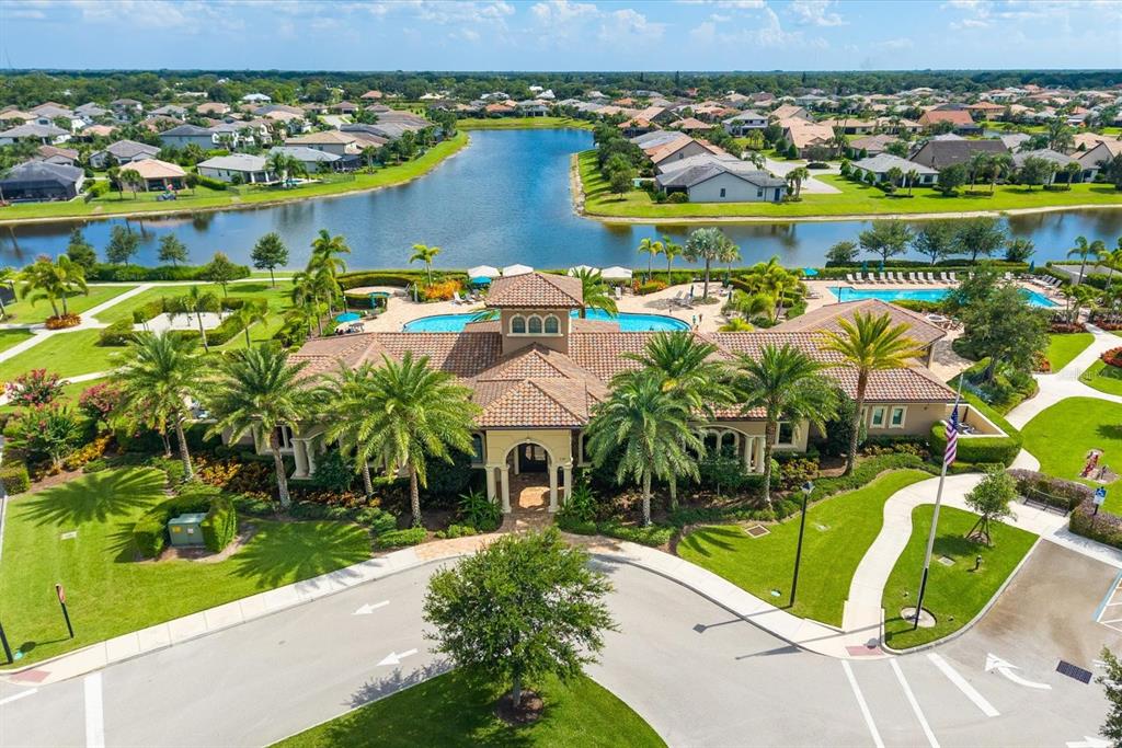 An aerial view shows a community clubhouse with a pool, palm trees, and a lake — 218 SE LONGVIEW DRIVE, PORT ST LUCIE, FL